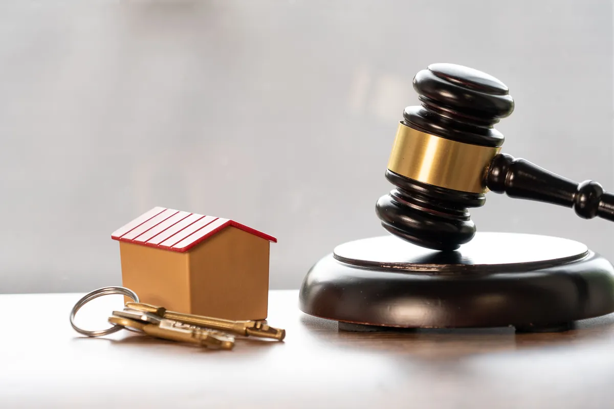Marteau de justice posé à côté d'une maquette de maison et d'un trousseau de clés, symbole du cadre juridique de l'immobilier