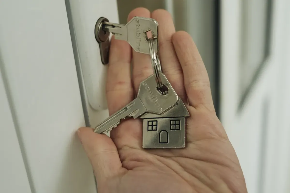 Main tenant un trousseau de clés avec un porte-clés en forme de maison devant une serrure
